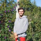 Reid stands in front a trellis of vines in the Community Garden